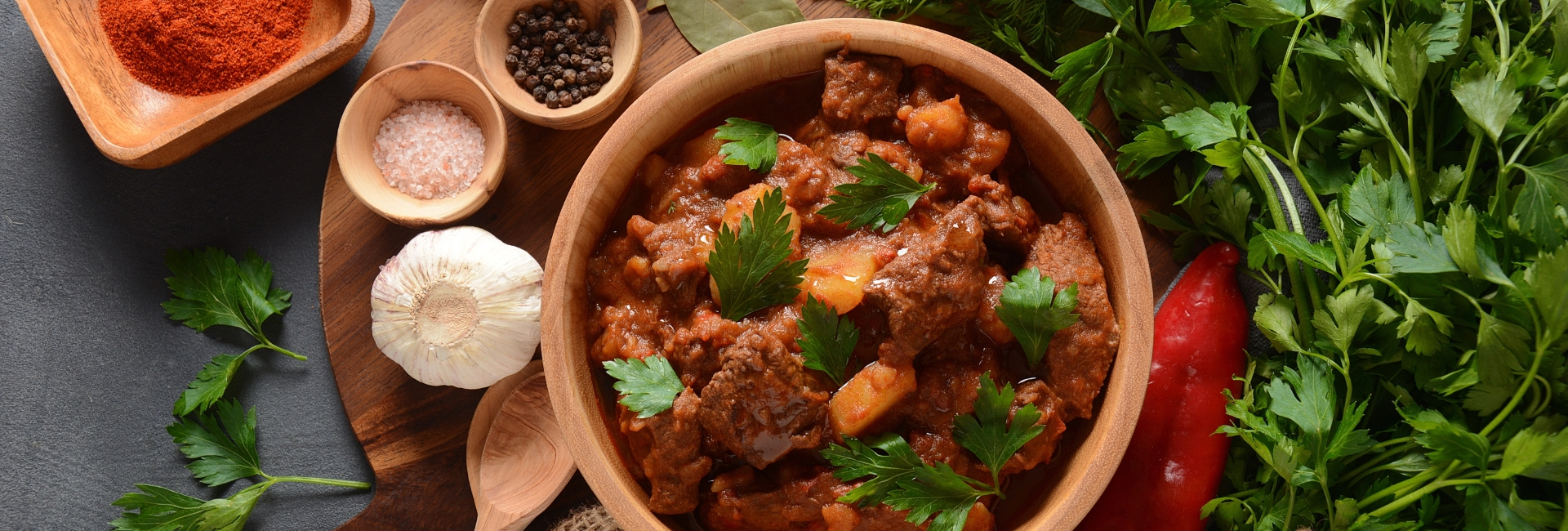 Pot of goulash surrounded by herbs and spices