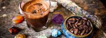 Cacao beans in blue bowl next to glass of cacao.