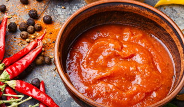 Hot sauce in a dish, chilli peppers alongside.